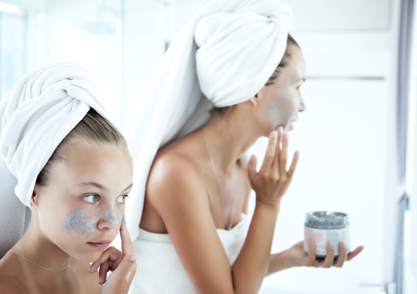 Woman and young woman with hair wrapped in white towels applying face masks