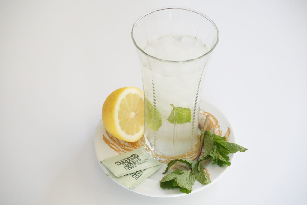 glass of fresh mint lemonade on plate with half lemon, stevia packets and mint leaves