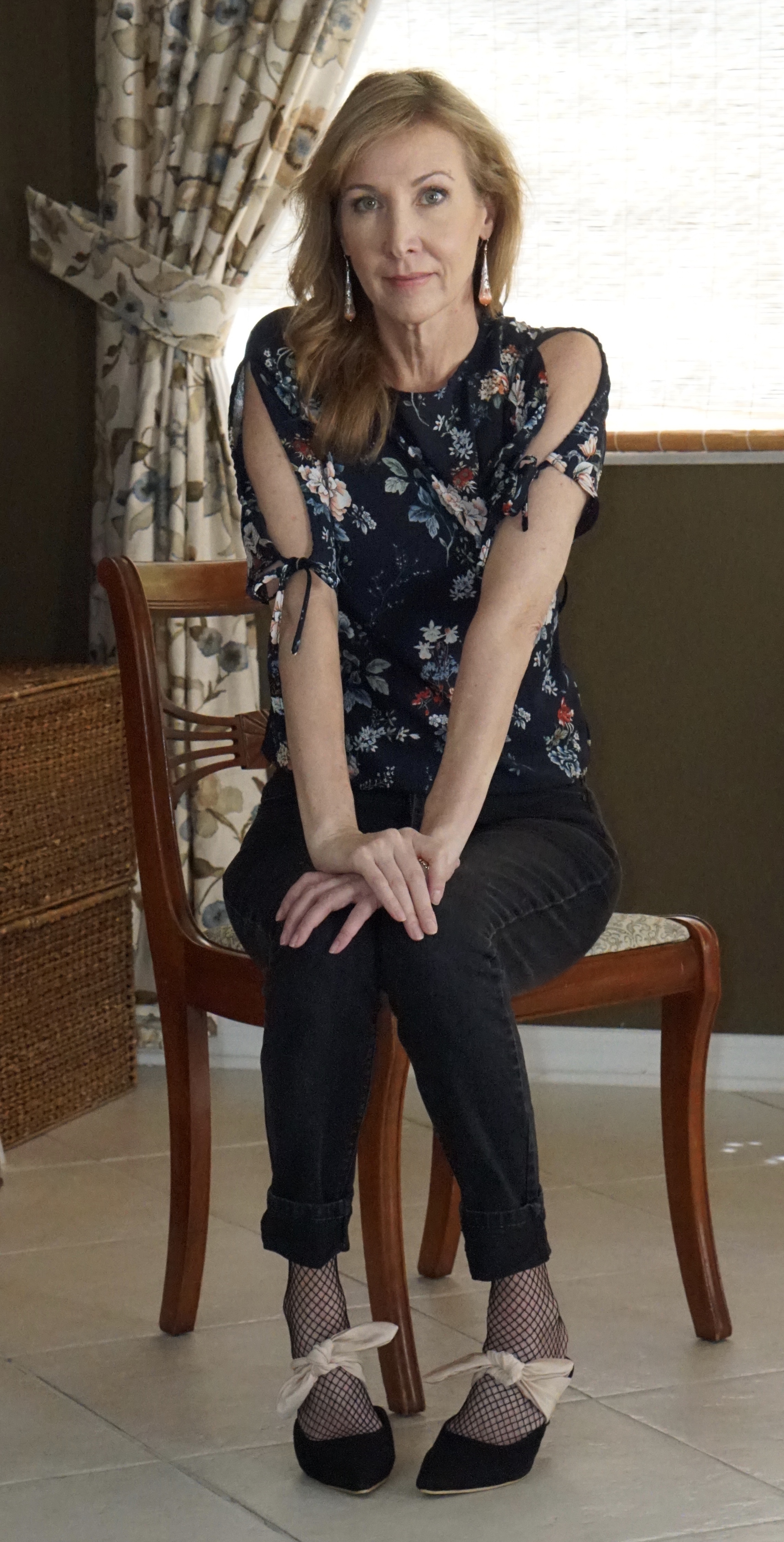 Woman sitting in chair wearing floral shirt and bow tie shoes