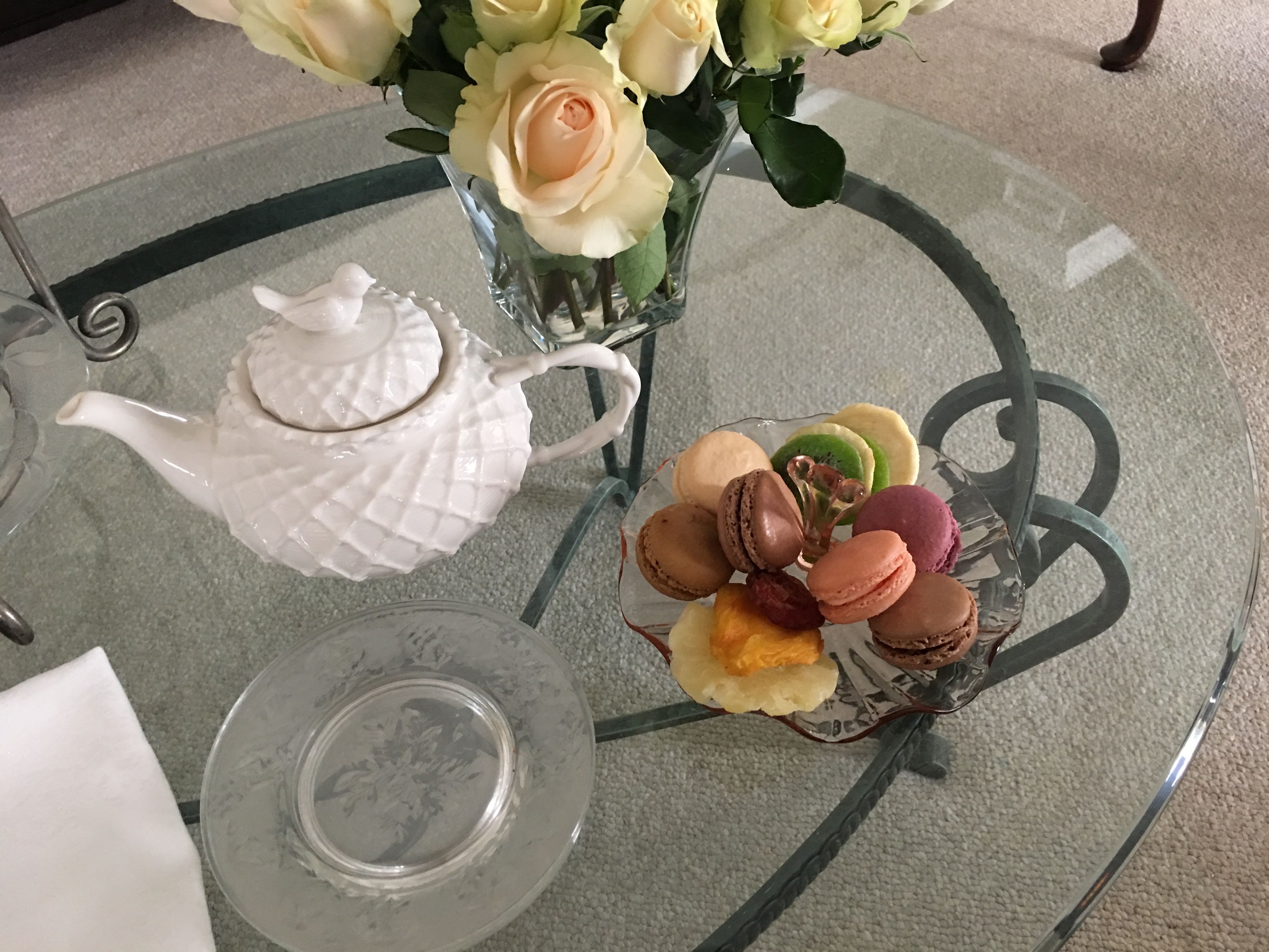 Glass table with white teapot, plate of macarons and vase of flowers