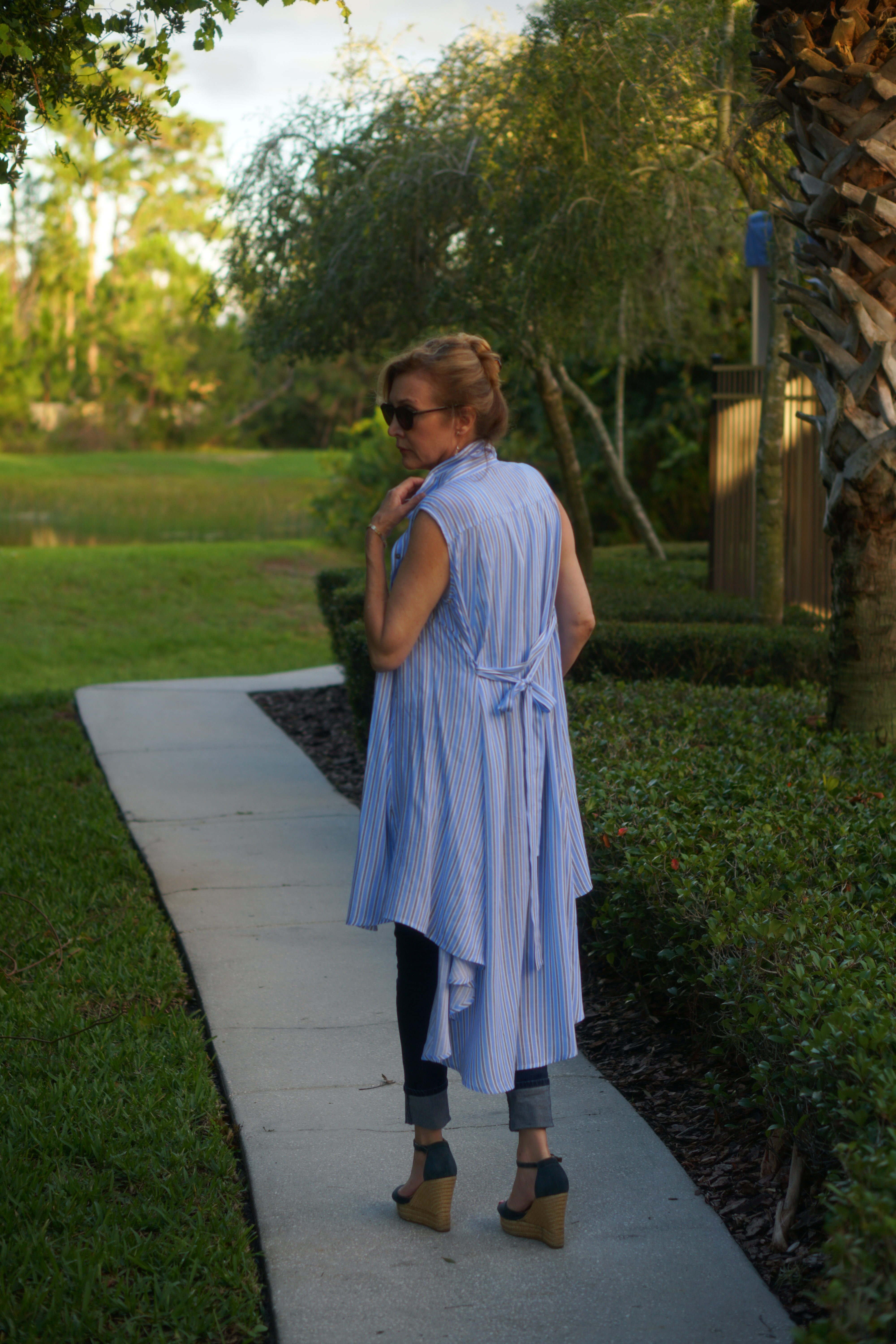 Woman wearing blue duster and wedge sandals walking down a path