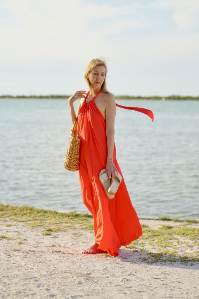 Beat the Heat by popular Florida life and style blog, Sharing a Journey: image of a woman wearing a red maxi dress and holding a pair of slide sandals and straw bag. 