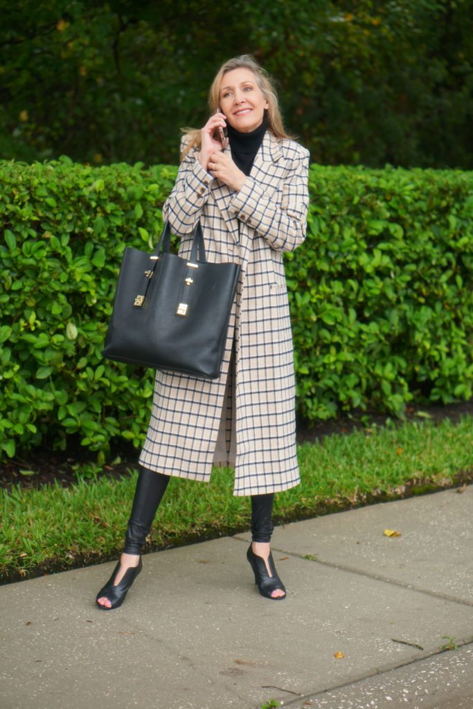 Woman wearing checkered long coat and large black tote bag