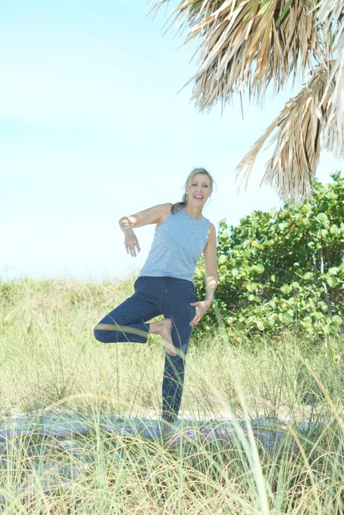 Nina from Sharing A Journey shares her complete guide to workout clothes for women over 50.  She is wearing a light blue yoga top and blue leopard print pants.
