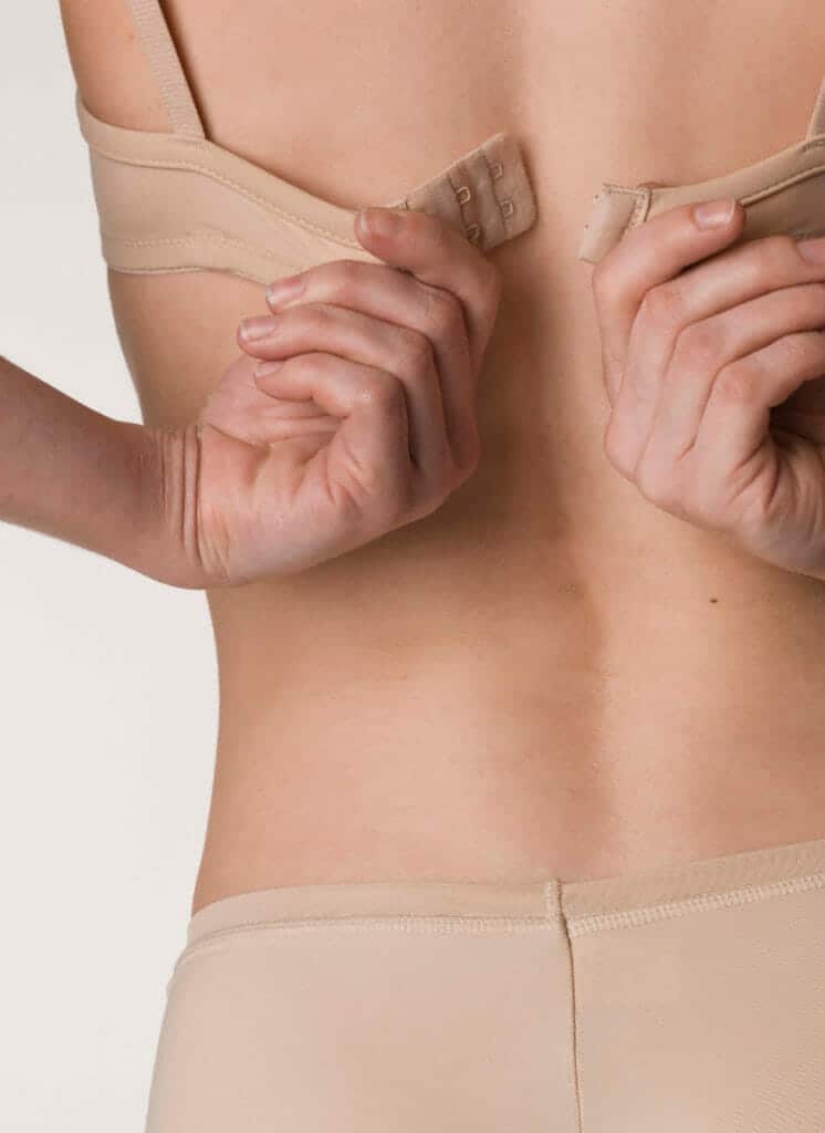 Woman holding clasps of beige bra wearing beige underwear