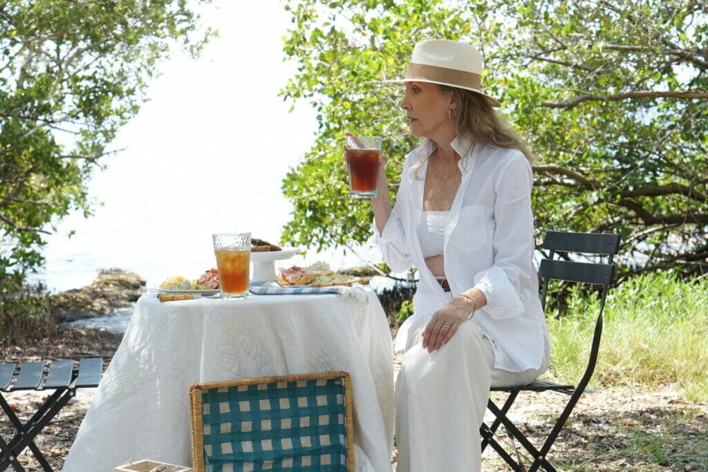 Woman sitting on chair, wearing white outfit having a picnic next to the water