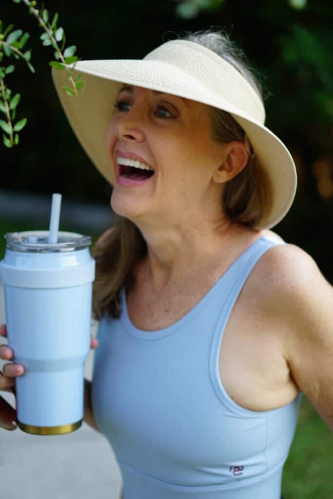 Laughing woman wearing a hat and a sports bra holding a water bottle