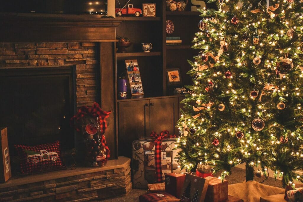 Lit up christmas tree with presents underneath next to a stone fireplace 