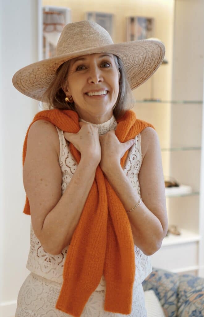 Nina Anders wearing hat, lace top and orange sweater 